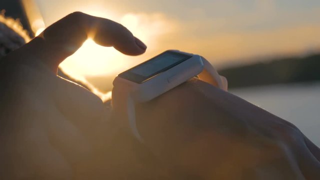 Woman using wearable smartwatch computer device on deck of cruise ship at sunset. Sunset light, sun lens flares, golden hour. Relax, nature and technology concept