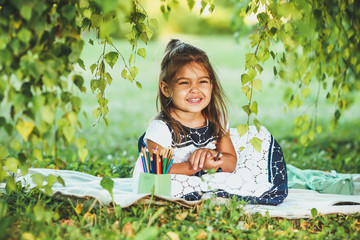 Happy little girl draws sitting on grass.