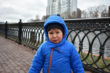 Little cute boy in blue dress is crying, offended by the embankment of the river