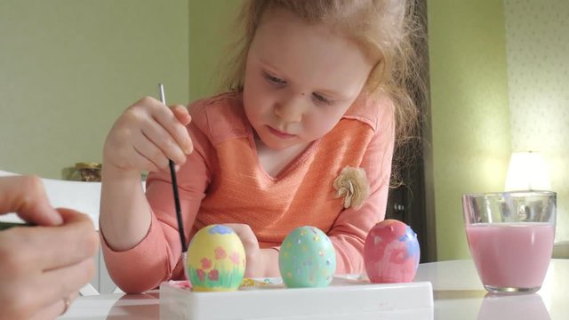 Mother and daughter draw Easter eggs with colored paints