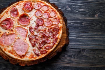 Pizza with bacon, salami,ham and pepperoni served on chopped wood, close up with copy space. Italian food, restaurant menu concept