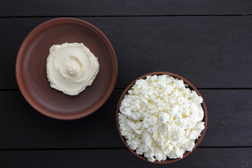 Cheese, fresh cottage cheese and sour cream in earthenware, goat curd on parchment paper, dairy products on a wooden background in rustic style, healthy food, copy space, dark background