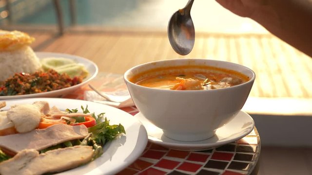 Shrimp soup is a Thai dish with a sour and spicy taste. the man is eating Tom Yam at a table by the pool. 4k, slow motion, close-up. concept of tourism tourism