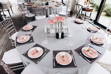 Wedding banquet table which is beautifully decorated in pastel colors, with white roses on plates,...