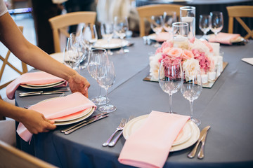 The process of decorating a festive table. Female hands spreads a pastel pink  napkins on the...