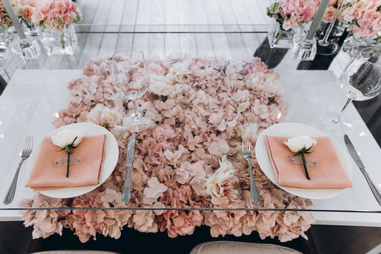 Banquet. Wedding. The glass table is decorated with a lot of beautiful pale pink flowers, with white roses on plates and pastel pink napkins