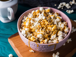 Popcorn with salted caramel in pink bowl on wooden board on dark background