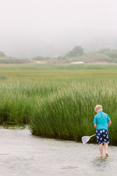 Per-teen boy fishing with a net in misty Cape Cod marshes