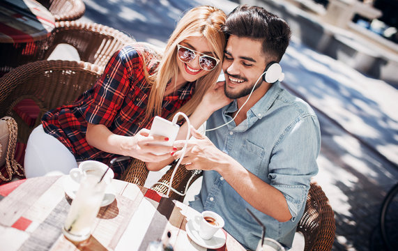 Dating. Young couple drinking coffee and having fun with mobile phone in the cafe. Love, dating, technology, lifestyle