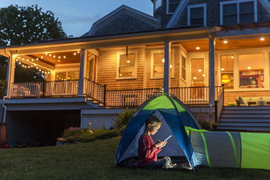 Boy using tablet while sitting in tent against illuminated house