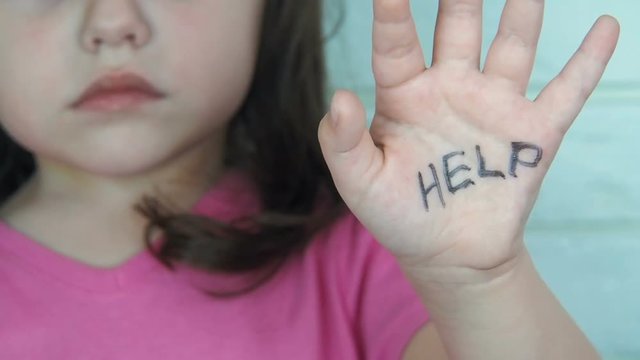 Child abuse. Domestic violence. A frightened child asks for help. A little girl shows an inscription on the palm of HELP.
