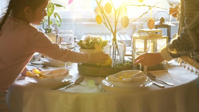 Young woman and her little daughter are setting easter festive table with bunny and eggs decoration. Slow Motion