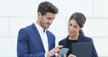 Businessman and businesswoman looking at cellphone together and business woman holding laptop computer at outdoor