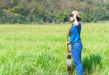 Woman wear hat and carry her guitar in grass field