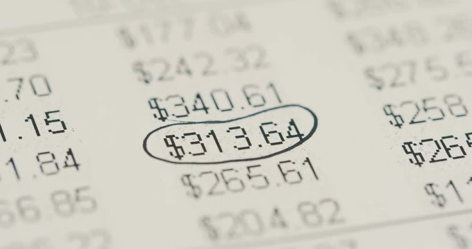 Close up of the table with numbers, currencies and per cents lying on the table and hand encircling them with black colour. Macro shooting