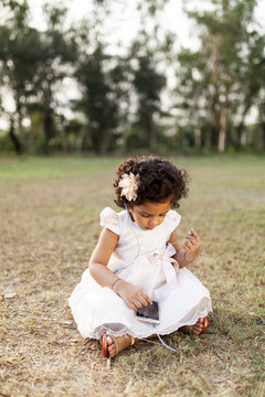 A kid sitting on grass,wearing white dress and listening music