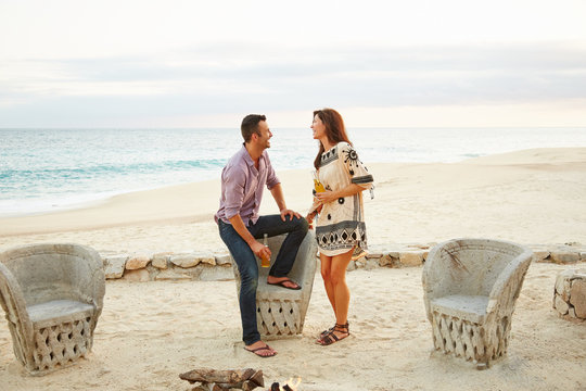 Couple enjoying a drink together by fire-pit on the beach on vacation