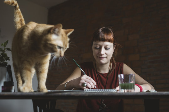 Woman artist painting in her studio with her cat
