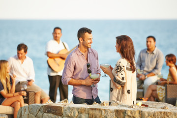 Friends having cocktails around a fire pit at the beach
