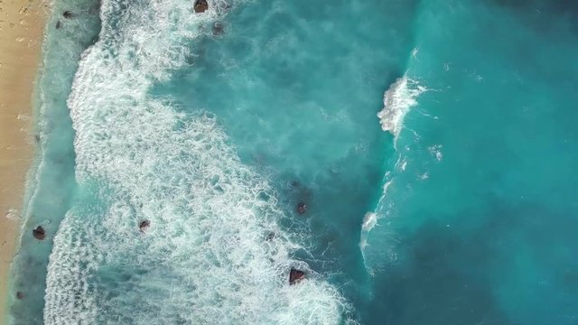 Aerial: Big Blue Waves Makes White Foam in Ocean near Sandy Beach. 4K. Nusa Penida, Bali, Indonesia.