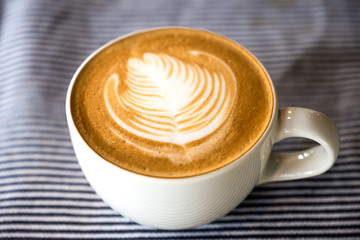 Closeup image of a cup of hot latte coffee with latte art on tablecloth