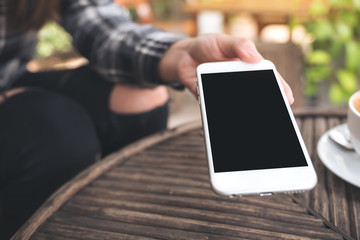 Mockup image of a hand holding and giving white mobile phone with blank black desktop screen to someone in cafe