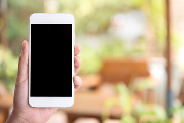 Mockup image of a hand holding and showing white smart phone with blank black desktop screen in outdoor with blur green nature background