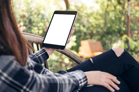 Mockup image of woman's hand holding black tablet pc with blank white screen while sitting outdoor with green nature background