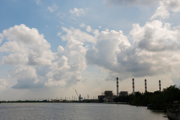 Power plant cooling tower and crane situated near the river with cloudy sky background