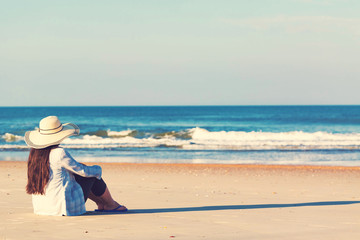 Fototapeta na wymiar Woman in a hat sitting on the beach toward sunset
