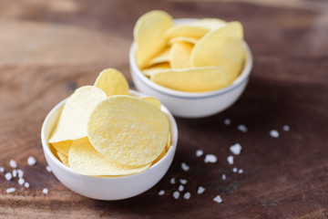 Potato chips in a bowl and salt on wooden background