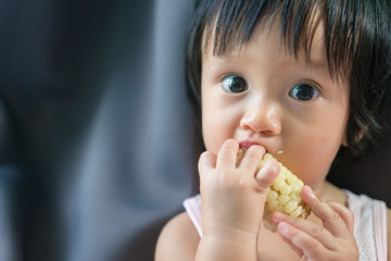 Asian baby eating corn and holding it by himself in day time