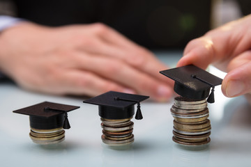 Businessperson Placing Graduation Hat Over Stacked Coins