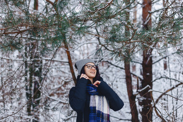 cute girl in glasses under pine branches with snow in winter in the forest