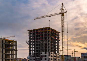 Building crane and building under construction. Construction site. Construction cranes and high rise building under construction against cloudy sky