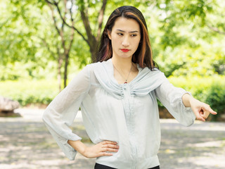 Beautiful young brunette Asian woman point at  something with another hand on waist. Outdoor...