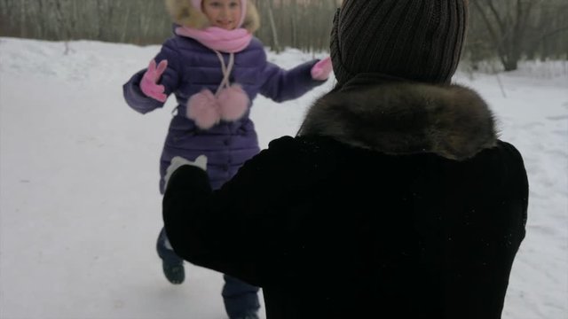 Young girl daughter runs to her mother by snow, hugs mom and kisses mother. Close up.