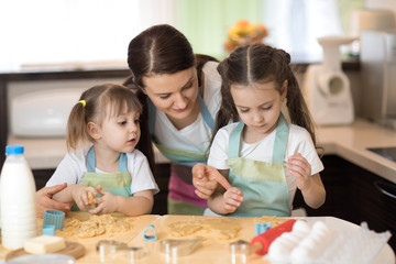Mom with her 2 and 5 years old daughters are cooking in the kitchen to Mothers day