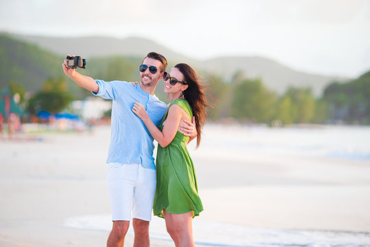 Selfie couple taking pictures on the beach. Tourists people taking travel photos on summer holidays.