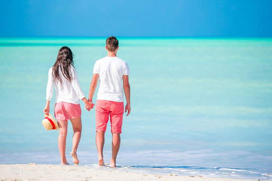 Young couple walking on tropical beach with white sand and turquoise ocean water at Antigua island in Caribbean