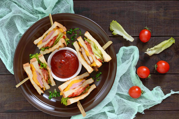 Club-sandwiches with crispy toast, sausage, cheese, tomato, greens. Traditional American snack.