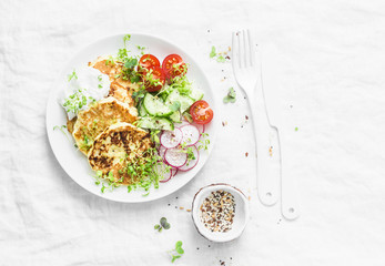 Ricotta zucchini fritters and fresh vegetables salad. Cucumbers, cherry tomatoes, radishes, micro greens and zucchini pancakes on light background, top view. Dietary breakfast or snack