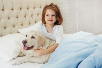 Beautiful little girl with golden retriever dog in a bed