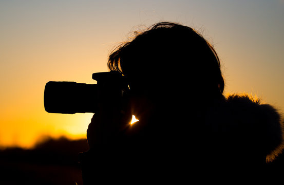 A girl is taking pictures with a camera at sunset
