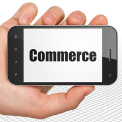 Business concept: Hand Holding Smartphone with black text Commerce on display, 3D rendering