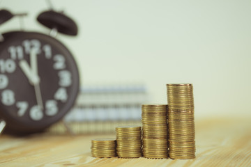 Steps of coins stack with vintage alarm clock and pen, notebook paper on wooden working table with copy space for text, financial and business planning concept. vintage tone..