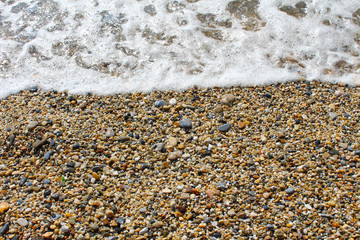 Pebble shore with sea foam of the wave