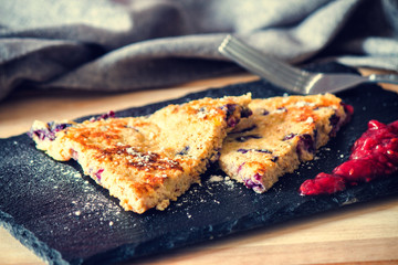 Banana and blueberry pancake with raspberry jam on a black plate with a fork.
