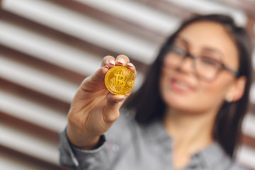 young successful confident woman with glasses holds a gold bitcoin in her hand