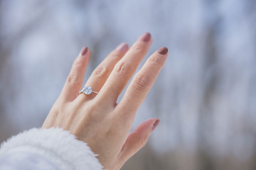 Close up of an elegant engagement diamond ring on woman finger with white sweater winter clothe background. love and wedding concept. soft and selective focus.